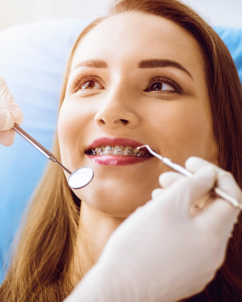 mulher-jovem-sorridente-com-suportes-ortodonticos-examinados-pelo-dentista-na-clinica-odontologica-ensolarada-dentes-saudaveis-e-conceito-de-medicina